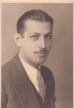 A dapper man in a suit, with a moustache, posing for a photo in sepia tones.